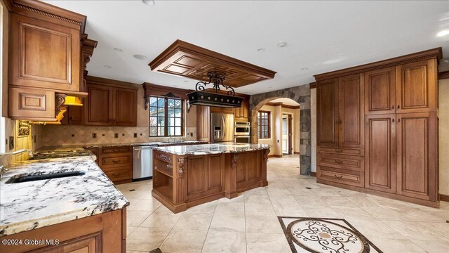 kitchen with light tile patterned flooring, sink, light stone countertops, appliances with stainless steel finishes, and a kitchen island