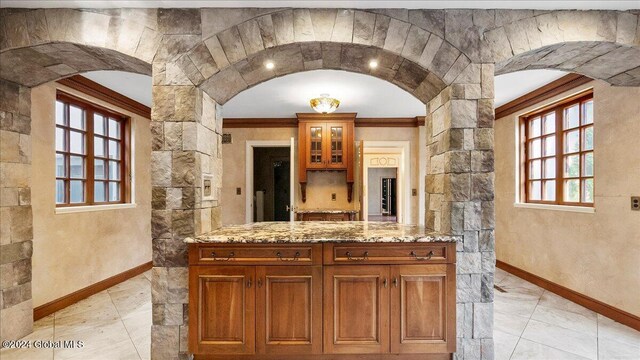 interior space with light stone countertops, a healthy amount of sunlight, and crown molding