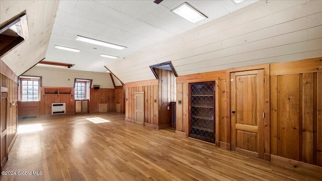 additional living space with wood walls, wood-type flooring, and heating unit