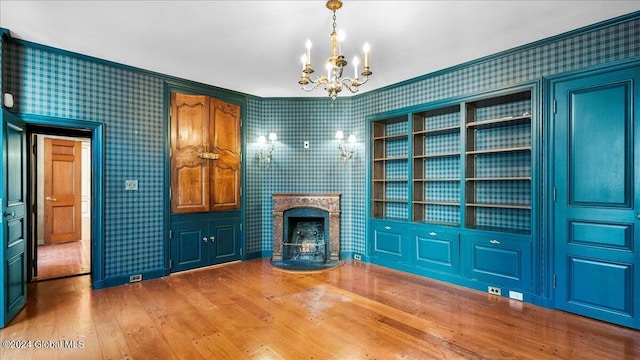 unfurnished living room featuring hardwood / wood-style floors, built in features, and a notable chandelier