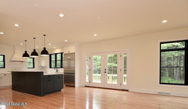 kitchen featuring light wood-type flooring, custom range hood, white cabinets, a kitchen island, and hanging light fixtures