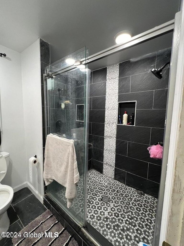 bathroom featuring tile patterned floors, toilet, and a shower with shower door