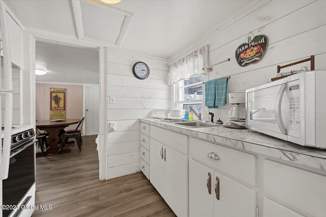 kitchen with dark hardwood / wood-style floors, wood walls, white cabinetry, sink, and stove