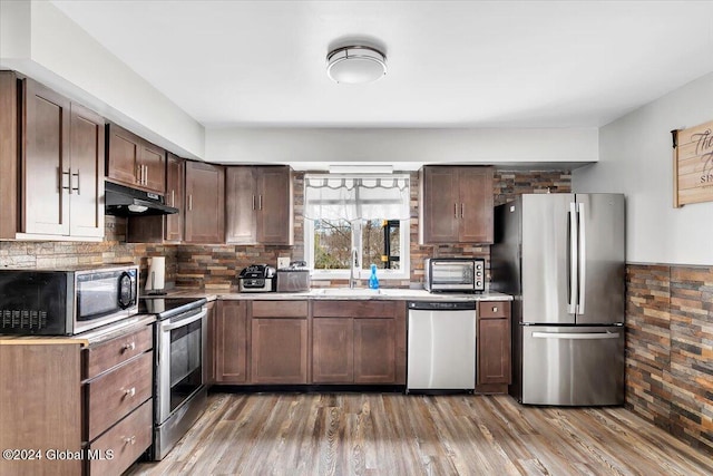 kitchen with dark brown cabinetry, sink, stainless steel appliances, tasteful backsplash, and hardwood / wood-style floors