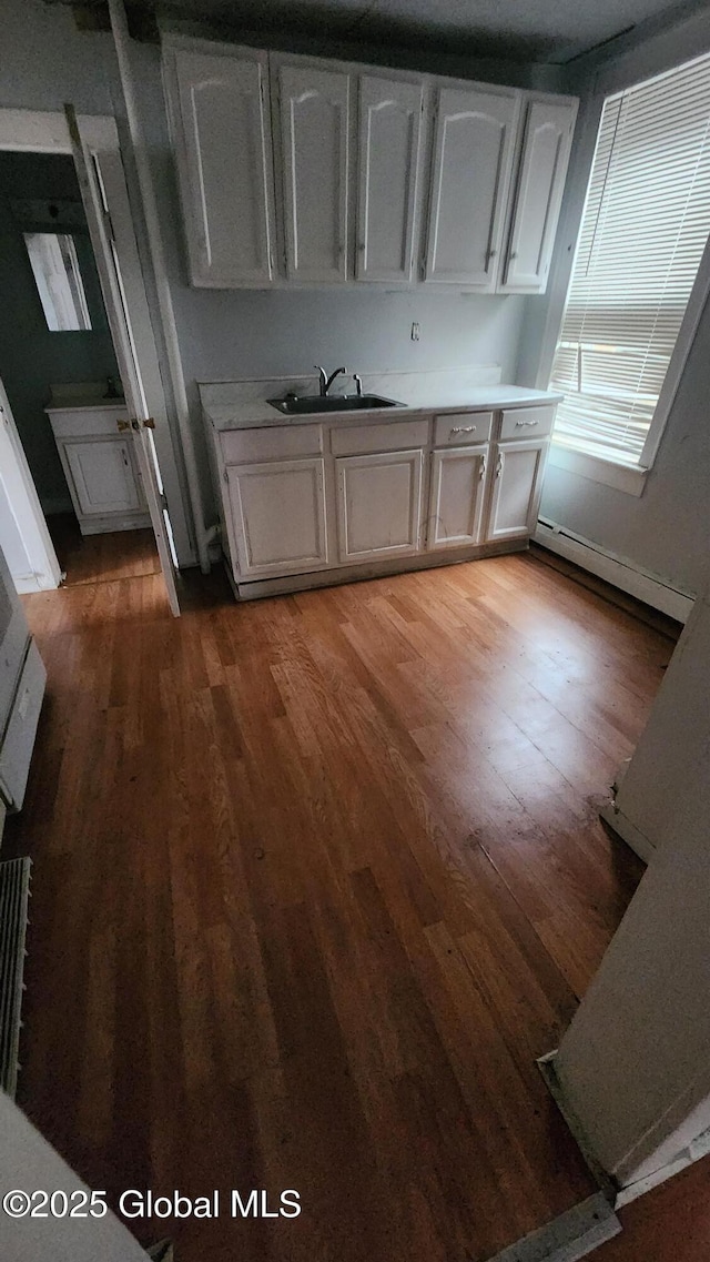 kitchen featuring wood-type flooring, white cabinetry, a baseboard heating unit, and sink