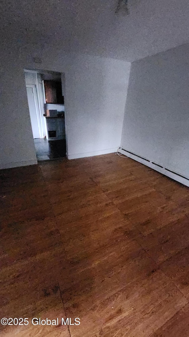 unfurnished room with dark hardwood / wood-style flooring and a baseboard heating unit