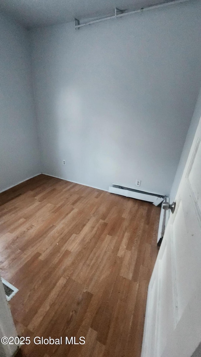 empty room with hardwood / wood-style floors and a baseboard heating unit