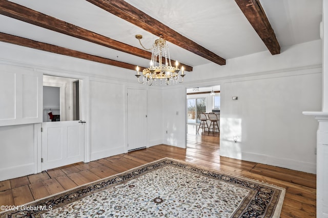 spare room featuring beam ceiling, hardwood / wood-style floors, and a notable chandelier