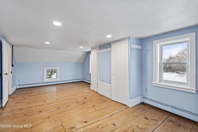 additional living space with lofted ceiling, a baseboard heating unit, and light hardwood / wood-style floors