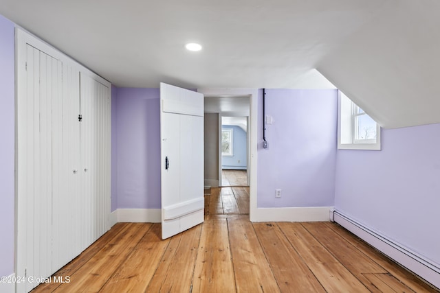 unfurnished bedroom featuring light hardwood / wood-style flooring, a closet, vaulted ceiling, and baseboard heating