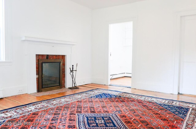 unfurnished living room featuring wood-type flooring, a brick fireplace, and baseboard heating