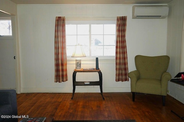 sitting room with a wall unit AC, dark wood-type flooring, and wood walls