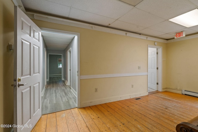 unfurnished room featuring light hardwood / wood-style floors, baseboard heating, and a drop ceiling