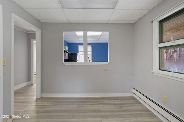 unfurnished room with a drop ceiling, a baseboard radiator, and light hardwood / wood-style floors