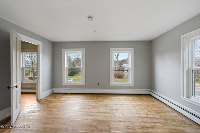 empty room with light wood-type flooring, a wealth of natural light, and a baseboard heating unit