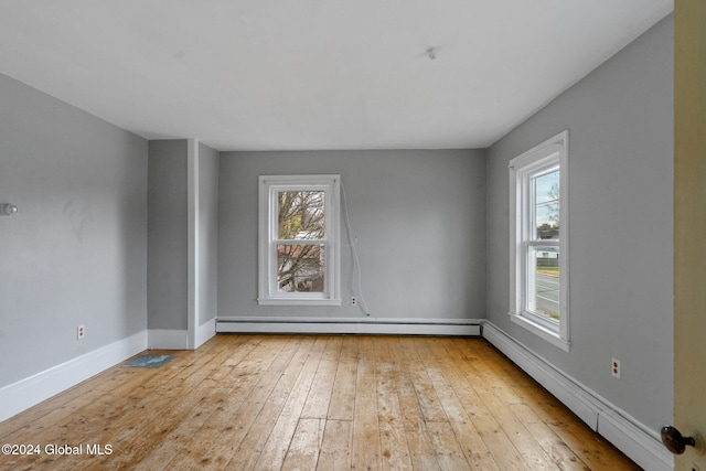 unfurnished room featuring light wood-type flooring, a wealth of natural light, and a baseboard heating unit