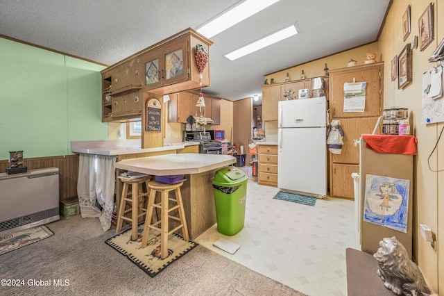 kitchen with a breakfast bar, wooden walls, a textured ceiling, white fridge, and kitchen peninsula