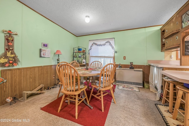 dining area featuring carpet flooring, a textured ceiling, and wooden walls