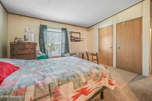 bedroom with carpet flooring, a textured ceiling, two closets, crown molding, and wooden walls