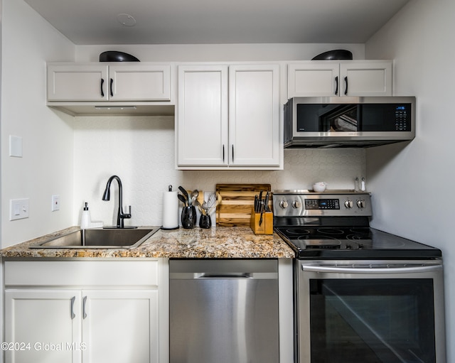 kitchen with backsplash, light stone counters, stainless steel appliances, sink, and white cabinetry