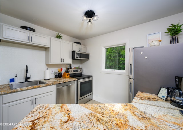 kitchen with white cabinets, appliances with stainless steel finishes, light stone countertops, and sink