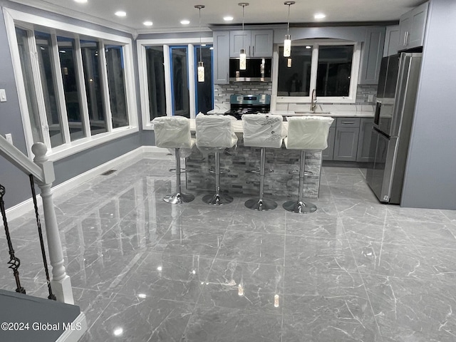 interior space with a kitchen breakfast bar, backsplash, stainless steel appliances, gray cabinets, and hanging light fixtures