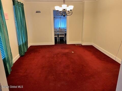 spare room with dark colored carpet, crown molding, and an inviting chandelier