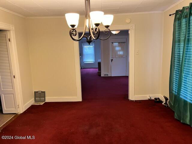 unfurnished dining area featuring dark carpet, ornamental molding, and a chandelier