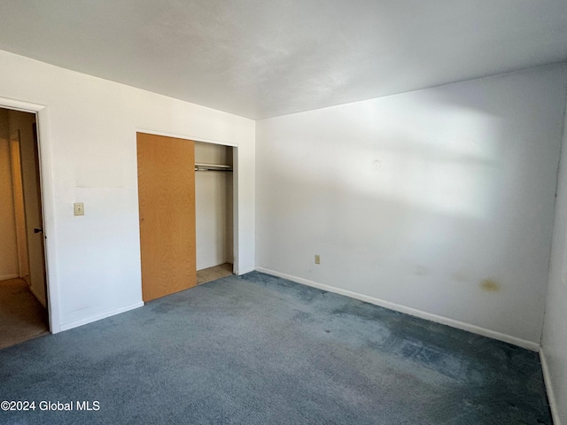 unfurnished bedroom with dark carpet and a closet