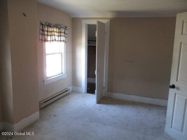 unfurnished bedroom with light colored carpet, a closet, and a baseboard heating unit