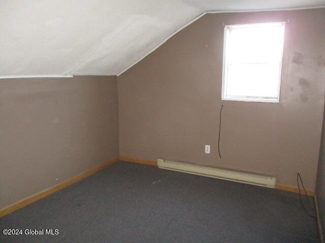 additional living space with a baseboard radiator, lofted ceiling, and dark carpet