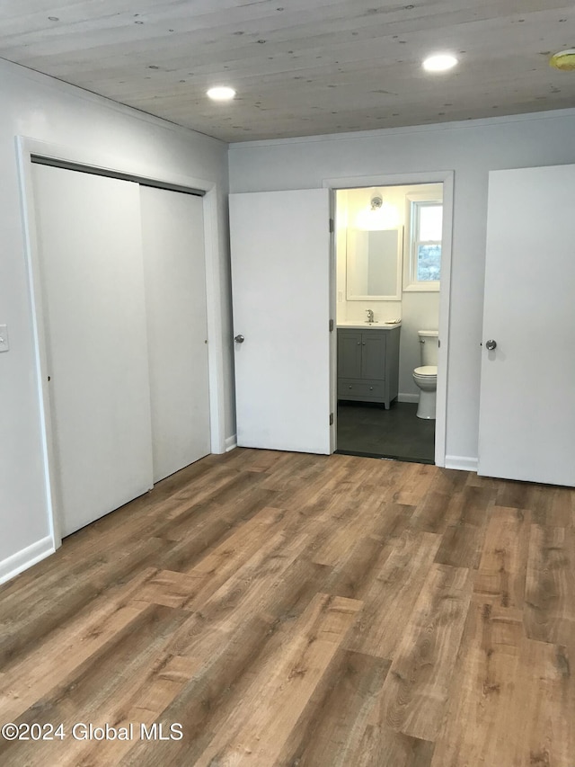 unfurnished bedroom with connected bathroom, a closet, wood-type flooring, and sink