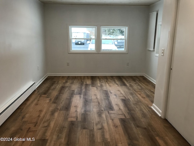 spare room featuring baseboard heating and dark wood-type flooring