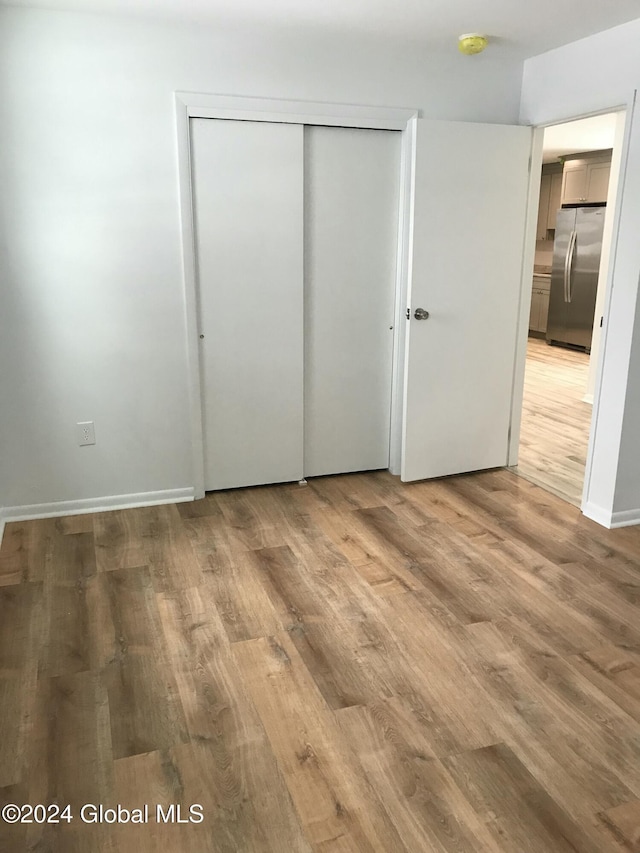 unfurnished bedroom with stainless steel refrigerator, a closet, and wood-type flooring