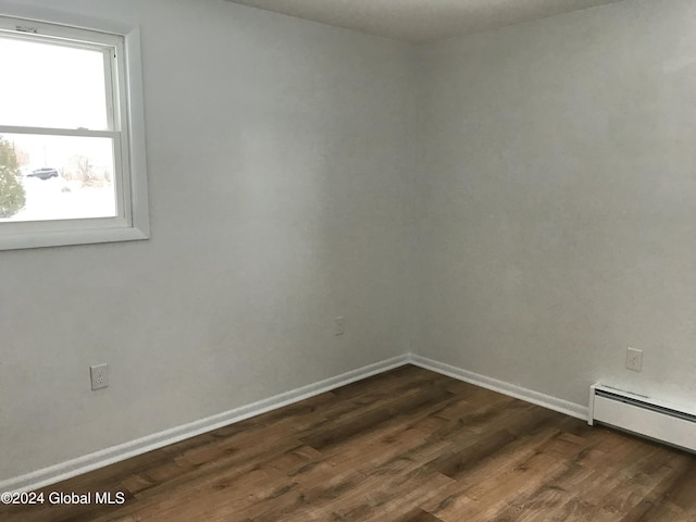 unfurnished room with dark hardwood / wood-style flooring and a baseboard heating unit