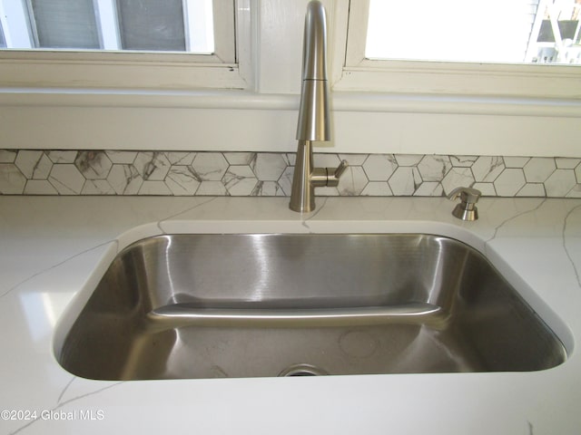 room details featuring decorative backsplash, light stone counters, and sink