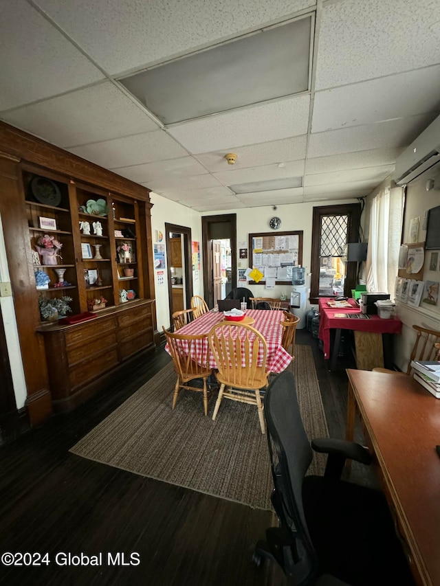 dining area with a wall unit AC, a drop ceiling, and dark wood-type flooring