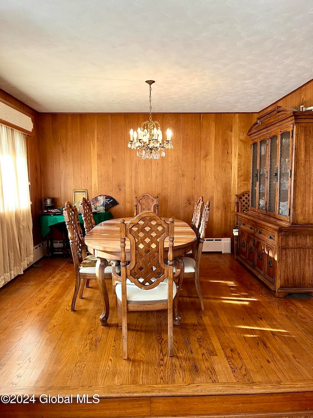 dining room with a chandelier, wooden walls, hardwood / wood-style flooring, and a baseboard heating unit