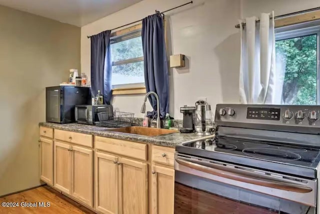 kitchen with electric stove, light brown cabinetry, sink, and light hardwood / wood-style flooring