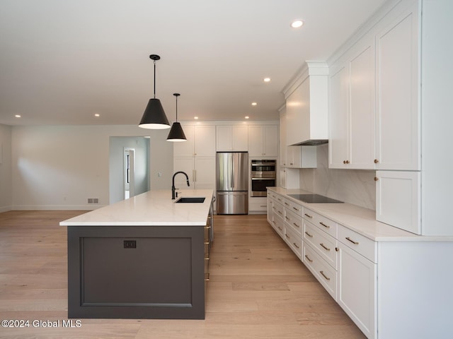 kitchen featuring white cabinetry, sink, stainless steel appliances, a kitchen island with sink, and light wood-type flooring