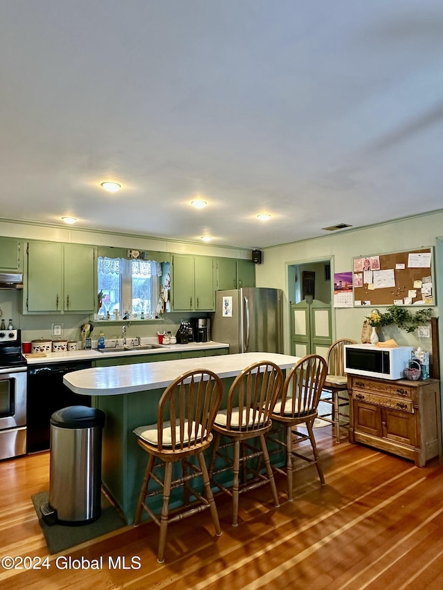 kitchen with a kitchen bar, green cabinets, hardwood / wood-style flooring, and appliances with stainless steel finishes