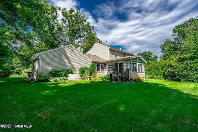 rear view of house featuring a sunroom and a lawn