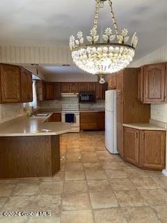 kitchen with white appliances, backsplash, sink, a notable chandelier, and kitchen peninsula