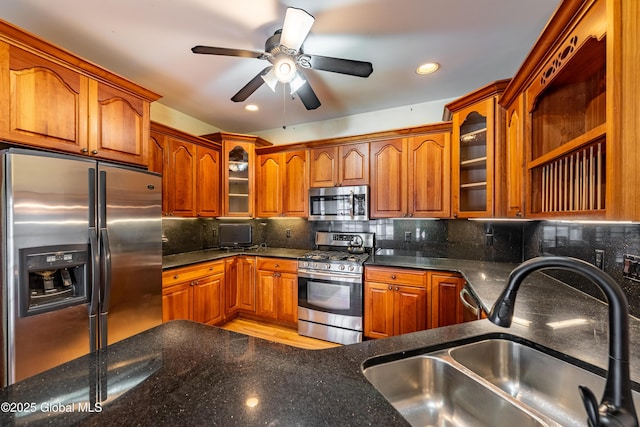 kitchen featuring appliances with stainless steel finishes, backsplash, ceiling fan, sink, and dark stone countertops