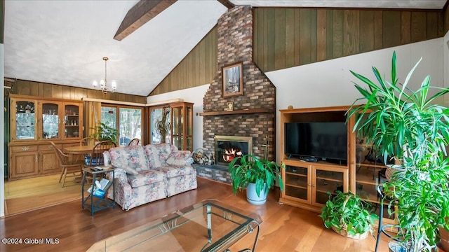 living room featuring a brick fireplace, light hardwood / wood-style flooring, high vaulted ceiling, a notable chandelier, and wooden walls