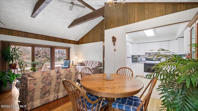 dining room with wood walls, light hardwood / wood-style flooring, ceiling fan, and high vaulted ceiling