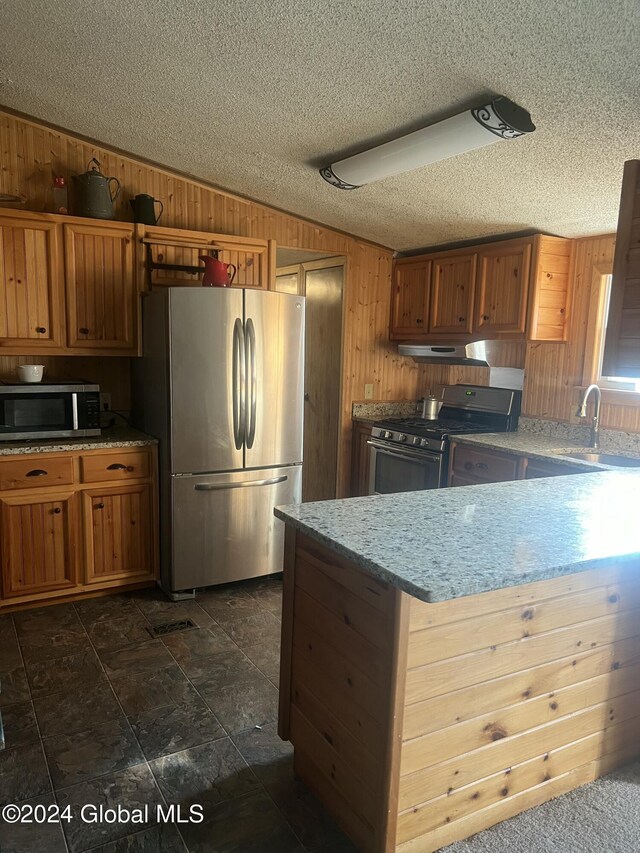 238 Mcewan Rd, Canajoharie, NY 13317 - kitchen with stainless steel appliances, wooden walls, exhaust hood, brown cabinets, and a textured ceiling