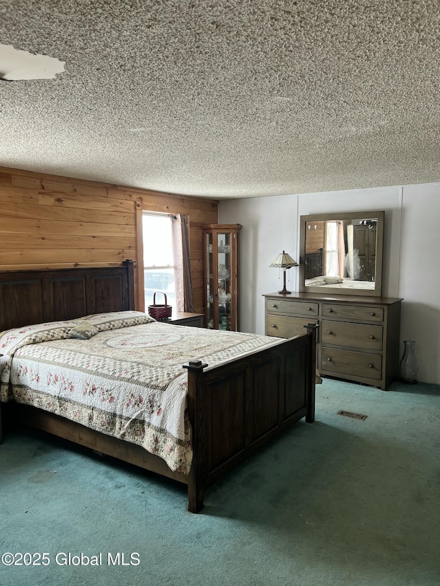 bedroom featuring visible vents, carpet, wooden walls, and a textured ceiling