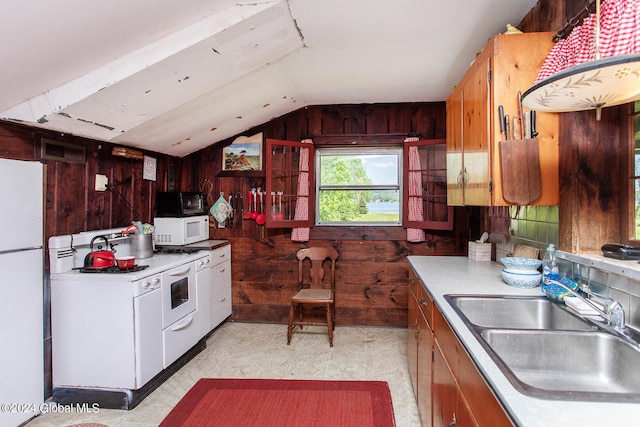 kitchen featuring wood walls, white appliances, lofted ceiling, and sink