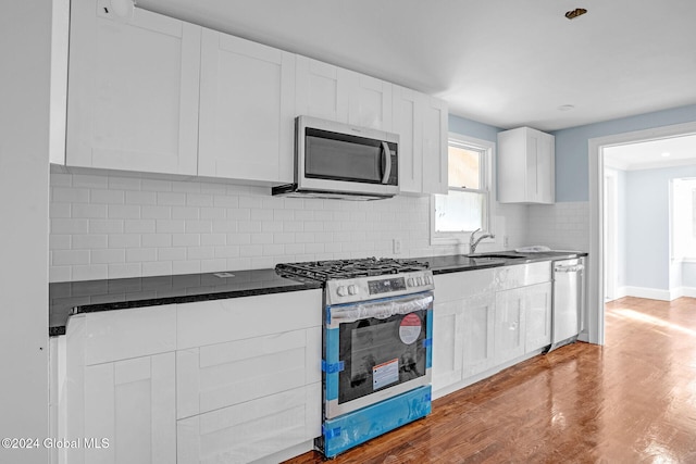 kitchen with sink, stainless steel appliances, backsplash, hardwood / wood-style floors, and white cabinets